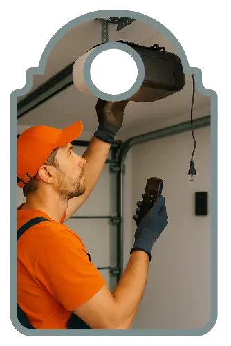 A technician in an orange uniform installs a modern garage door opener unit on a ceiling mount while holding a remote control in a clean residential garage.